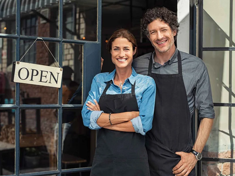 A husband and wife stand in front of their storefront needing Tax and Accounting services for their new business.