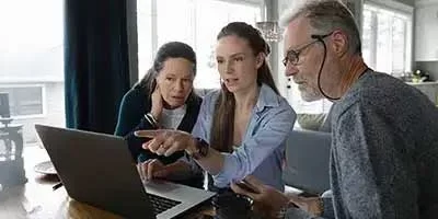 Retirement Taxes: No surprises: What Boomers Need to Know Before It’s Too Late. Two seniors and a younger woman look at a laptop in discussions.