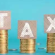Stacks of coins with blocks spelling "TAX" on a blue background - representing the 2025 Tax Changes