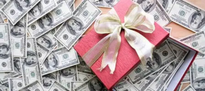 A pink gift box with a ribbon sits on a pile of US dollar bills representing Qualified Charitable Distributions